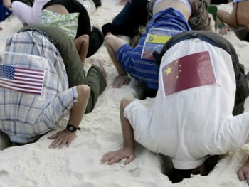 Các nhà hoạt động vì môi trường ở Cancun mặc áo có dán hình quốc kỳ các nước, đâm đầu vào cát để biểu thị việc các nước nhắm mắt làm ngơ trước hậu quả của biến đổi khí hậu - Ảnh: Reuters